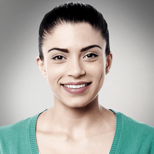 Woman with dark hair pulled back, smiling, wearing a green sweater against a gray background.