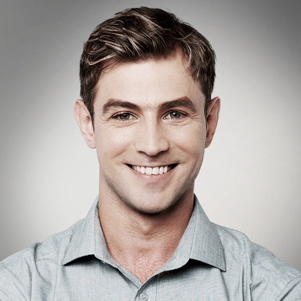 Smiling man with light brown hair in a light blue button-down shirt, neutral background.
